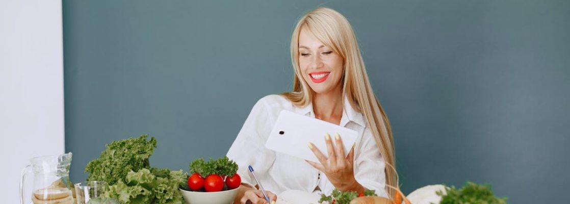 Woman using a tablet surrounded by fresh vegetables at a table, showcasing healthy lifestyle and technology.